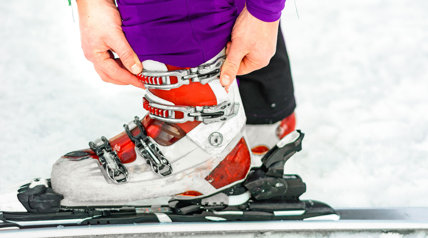 Gros plan sur les mains d'un adulte aidant un enfant à ajuster les boucles de sa chaussure de ski colorée