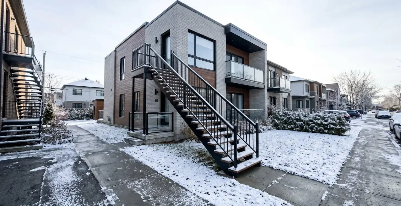 Un escalier extérieur résidentiel moderne équipé d'une rampe métallique noire sous une fine couche de neige, dans un quartier contemporain de la région montréalaise
