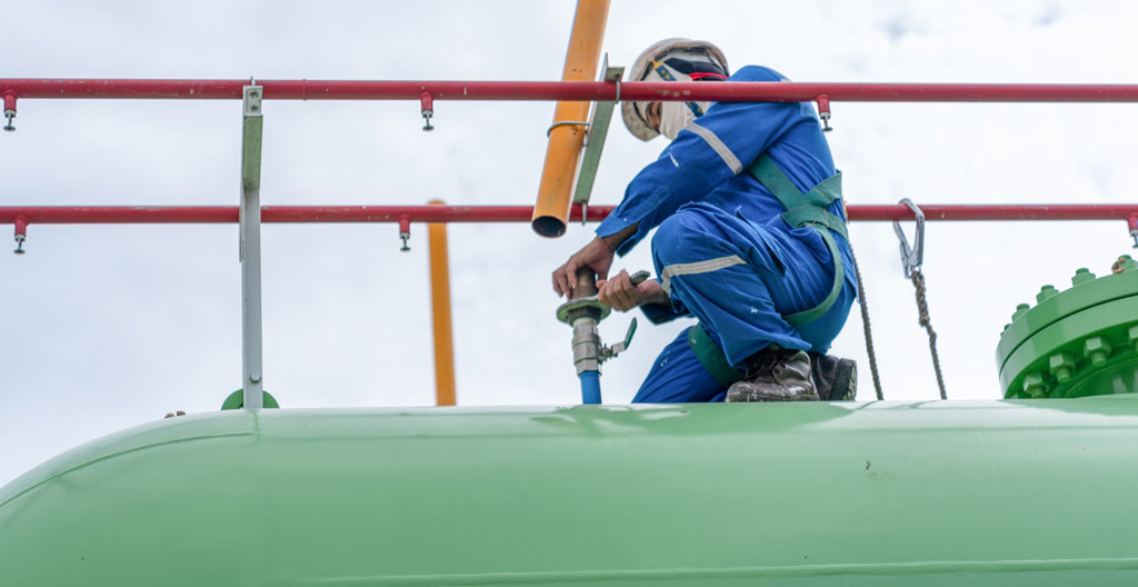 Technicien réalisant un contrôle technique sur une citerne de gaz propane installée à l'extérieur d'un bâtiment professionnel